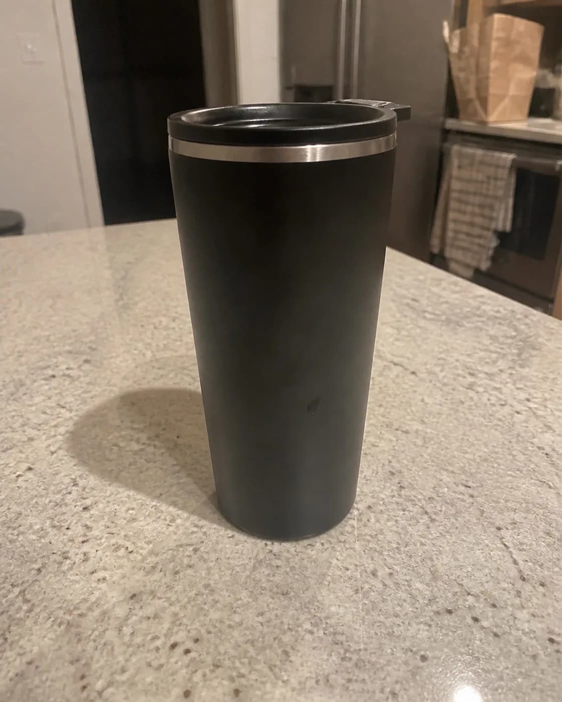 An ordinary phone photo of a black insulated tumbler on a kitchen counter